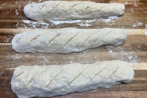 Tres baguettes de masa cruda con harina sobre una tabla
