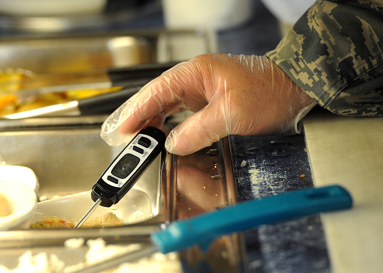 Manipulador con guantes midiendo la temperatura de un alimento con un termómetro