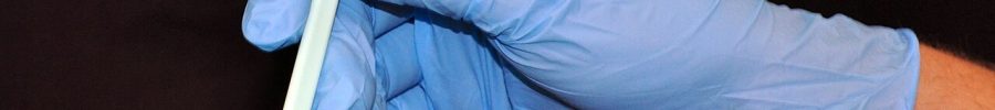 Mano con guante de nitrilo azul sosteniendo un hisopo
