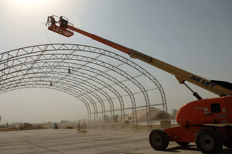 Plataforma elevadora de brazo telescópico con la cesta en altura junto a una estructura metálica